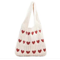 a white knitted bag with red hearts on the front and bottom, hanging from a hook