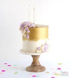 a white and gold cake with purple flowers on the top is surrounded by confetti