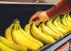 a person reaching for some bananas in a bin at a store or restaurant, with other items on the shelf behind them