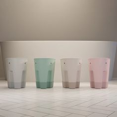 four different colored cups sitting on top of a white tiled floor