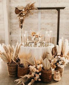 a table topped with lots of flowers next to tall candles and wicker baskets filled with feathers