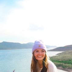 a woman is standing by the water with flowers in her hand and smiling at the camera