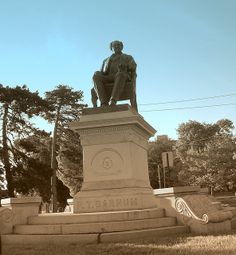 a statue of a man sitting on top of a pedestal in the middle of a park