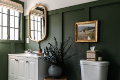 a white toilet sitting next to a bathroom sink under a mirror on a green wall