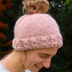 a woman wearing a pink knitted hat with a knot at the top, looking down