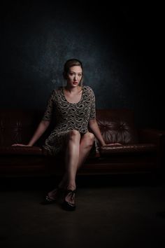 a woman sitting on top of a couch in a dark room with her legs crossed