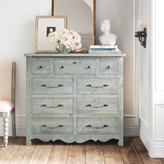 an old dresser with flowers on top and a mirror in the corner next to it