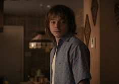 a young man standing in a kitchen looking at the camera with an intense look on his face