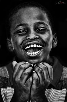 a black and white photo of a young boy with his hands on his chest smiling