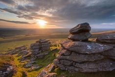 the sun is setting over some rocks on top of a hill