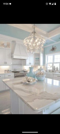 a large kitchen with white cabinets and marble counter tops, chandelier above the island