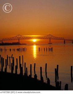 the sun is setting over the water with a large bridge in the distance behind it