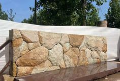 a large rock wall sitting on top of a cement slab next to a wooden fence