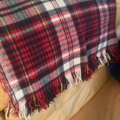 a red and black plaid blanket sitting on top of a couch next to a pillow