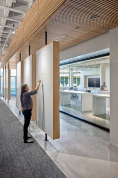 a person standing next to a white board in an office building with lots of windows