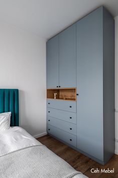 a bed sitting next to a tall blue cabinet in a room with wooden floors and white walls