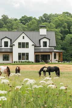 four horses graze in front of a large white house surrounded by trees and grass