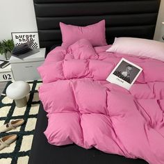 there is a pink comforter on the bed with shoes and a book next to it