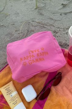 a pink bag sitting on top of a towel next to sunglasses and sunscreenr