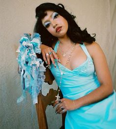 a woman in a blue dress sitting on a chair with her hand on the arm