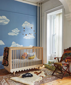 a baby's room decorated in blue and white with clouds painted on the wall