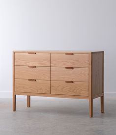 a wooden dresser with six drawers and two handles on each drawer, against a white wall