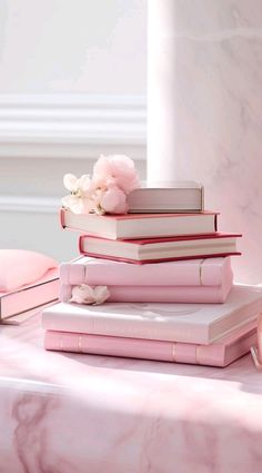 a stack of pink books sitting on top of a table next to a vase with flowers