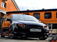 a black car is parked in front of a house with an orange train behind it