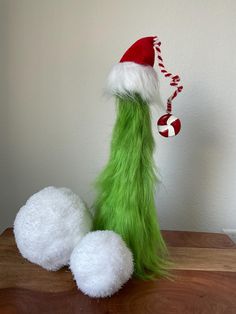 a green and white stuffed animal wearing a santa hat on top of a wooden table