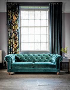 a green velvet couch sitting in front of a window