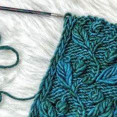 a close up of a knitting needle and a green knitted blanket with leaves on it