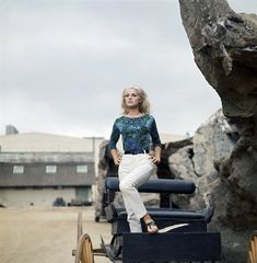 a woman sitting on top of a wooden cart next to a large rock and building