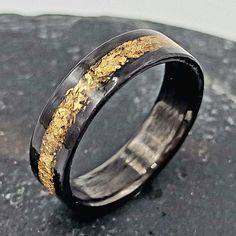 a black and gold wedding ring on top of a stone slab with some gold flakes in it