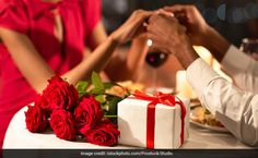 two people sitting at a table holding hands over a gift box with red roses on it