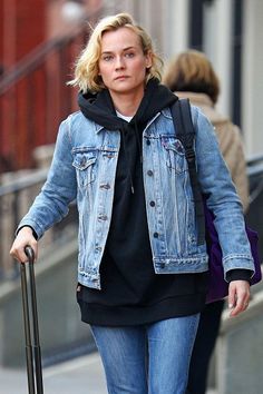 a woman walking down the street with her luggage and wearing a jean jacket over her shoulders