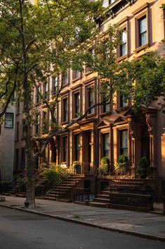 a row of brownstone townhouses on a city street with trees in the foreground