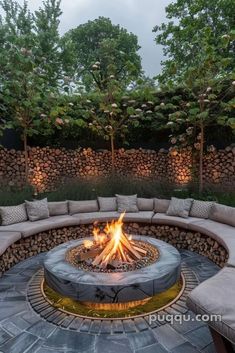 an outdoor fire pit surrounded by stone walls and seating area with trees in the background