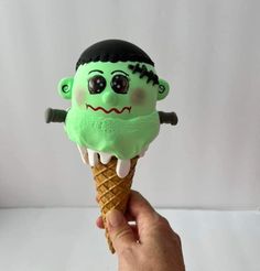 a hand holding an ice cream cone with a green monster on it's head