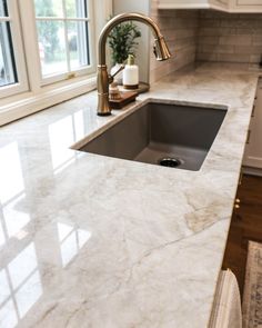 a kitchen with marble counter tops and stainless steel faucet, white cabinets and windows