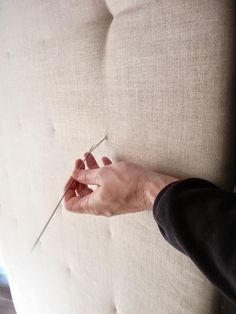 a person is holding something in their hand on the back of a couch with nails stuck to it