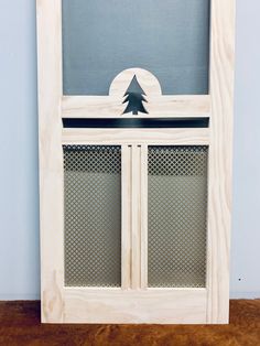 a white cabinet with a pine tree on the top and bottom panel, in front of a blue wall