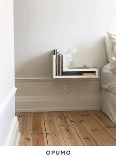 there is a shelf with books on it next to a bed in the room that has white walls and wood floors