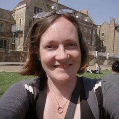 a woman wearing sunglasses is sitting in front of a building and smiling at the camera