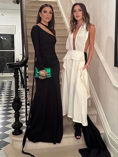 two women standing next to each other in front of a stair case, one wearing a black and white dress