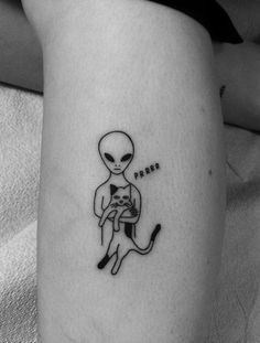 an alien holding a cat tattoo on the left side of the leg, with words written below it