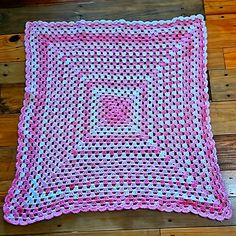 a pink and white crocheted square sitting on top of a wooden floor