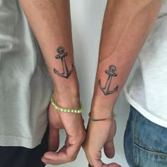 two people are holding hands with tattoos on their arms and one has an anchor tattoo