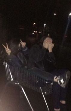 two people sitting in a shopping cart with their hands up to their face and one person covering their eyes