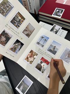 a person is holding a book with pictures on it and writing in a pen while sitting at a table