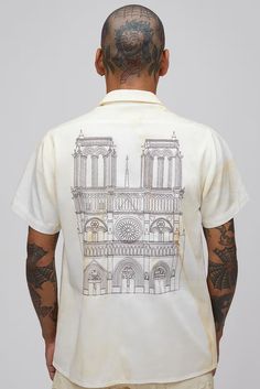 the back of a man with tattoos wearing a white shirt that has a drawing of a cathedral on it